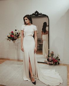 a woman standing in front of a mirror wearing a white dress with high slits