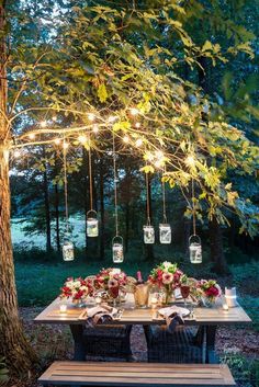 a picnic table with mason jars hanging from the branches and flowers on it, surrounded by greenery