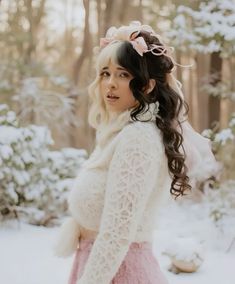 a woman with long hair wearing a white sweater and pink skirt standing in the snow