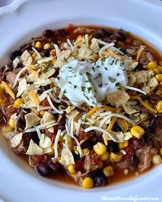 a white bowl filled with beans, corn and sour cream on top of tortilla chips