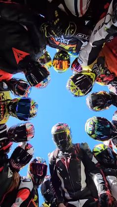 a group of motorcyclists standing in a circle looking up at the sky