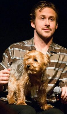 a man holding a small dog in his lap while sitting on a chair at an event