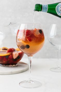 a person pouring wine into a glass with fruit in the bowl next to it on a white table