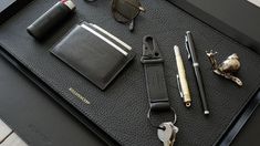 an assortment of personal items laid out on a black leather tray with sunglasses, pen and lighter