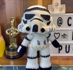 a crocheted star wars character is posed next to a trophy on a shelf