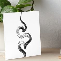 a black and white drawing of a snake on a white card next to a potted plant