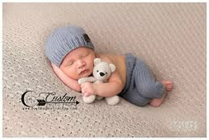 a baby sleeping with a teddy bear on top of it's back and wearing a knitted hat