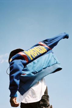 a man flying through the air while wearing a blue and yellow jacket on top of his head