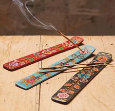 three incense sticks with colorful designs on them sitting on a wooden table next to two matchesticks