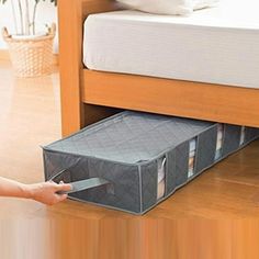 a person holding a piece of luggage in front of a bed with its drawers open