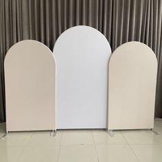 three white arches are next to each other in front of a curtained wall with drapes