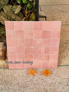 two orange stars are sitting on the ground next to a pink tile wall with words