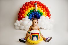 a baby sitting in front of a rainbow cake