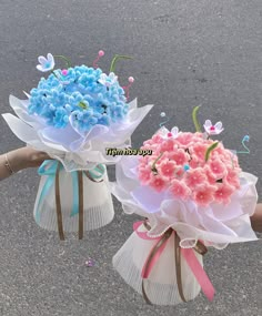 two vases filled with flowers sitting on the side of a road next to each other