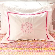 two white pillows with pink trim and monogrammed letters on them sitting on a bed