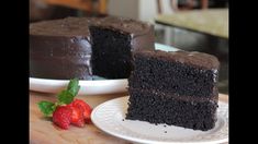 a slice of chocolate cake on a white plate with a strawberry next to it and another piece in the background