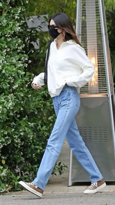 a woman in white shirt and jeans walking past a metal object with flame coming out of it