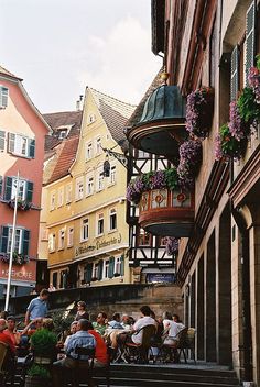 many people are sitting at tables in front of some tall buildings with flowers on them