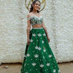 a woman standing in front of a white wall wearing a green lehenga and crop top