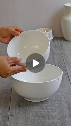 two hands holding white bowls on top of a wooden table