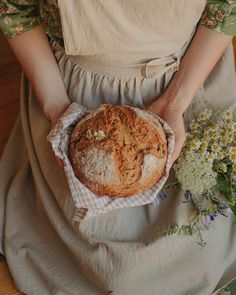 a woman holding a loaf of bread on top of a table next to some flowers