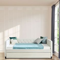 a white daybed with blue pillows in a living room next to a large window