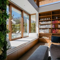 a living room filled with lots of books and furniture next to a window covered in plants