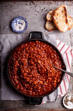 a skillet filled with baked beans next to bread and butter on a table top