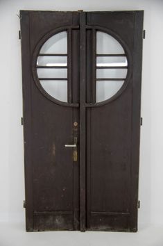 an old wooden door with two circular windows on the top and bottom part, in front of a white wall