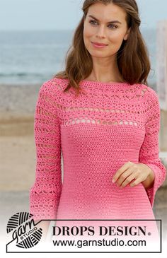 a woman standing on the beach wearing a pink crochet sweater