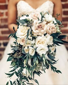 a bridal holding a bouquet of white roses and greenery in front of a brick wall