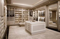 a large walk in closet with lots of clothes on shelves and white counter top drawers