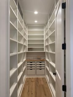 an empty walk - in closet with white shelves and wooden flooring, along with drawers