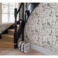 there are books on the floor in front of the stair case and wall papered with newspaper