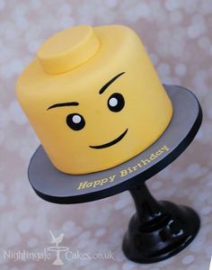 a yellow lego head cake sitting on top of a black plate with the words happy birthday written on it