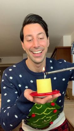 a man holding a small candle on top of a red plate in front of a christmas tree