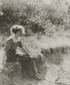 an old black and white photo of a woman sitting on the edge of a stream