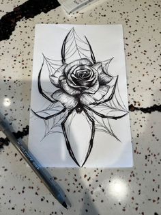 a black and white drawing of a rose on paper next to a marker with a pen