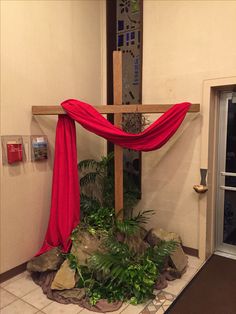 a cross with red cloth draped over it in front of a wall and door way