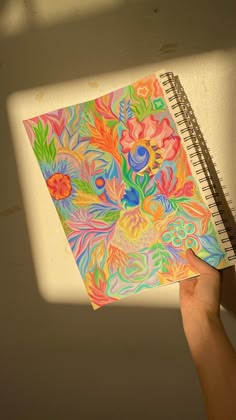 a hand holding a spiral notebook with an abstract painting on it