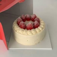 there is a cake with white frosting and strawberries on the top, sitting in a box