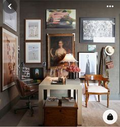 a room with many pictures on the wall and a desk in front of it that has a lamp