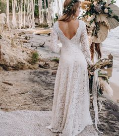 a woman in a wedding dress standing on the beach with her back to the camera