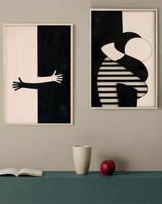 two framed art pieces hang on the wall above a table with an apple and coffee cup