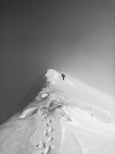 a person walking up the side of a snow covered mountain with footprints in the snow