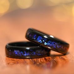 two wedding rings with blue and purple glitters on them sitting on a wooden surface