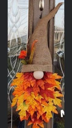 a scarecrow door hanger with fall leaves and an egg in the top hat