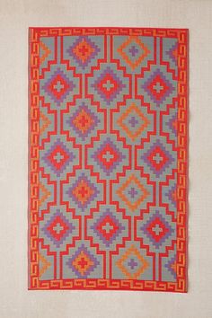 an orange, blue and red rug on a white wall