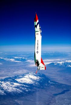 a multicolored jet flying through the sky above some snowcapped mountains and blue skies