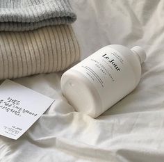 a bottle of lotion sitting on top of a bed next to some sweaters